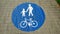 Symbol of a man holding a girl together with bicycle in blue circle depicting this is the zone for walking and riding bicycle