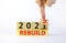 Symbol of planning 2022 rebuild new year. Businessman turns a wooden cube and changes words `rebuild 2021` to `rebuild 2022`.