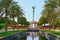 Symmetric park view to marble arabesque gazebo,fountain and elaborate girl sculpture -tightrope walker on hula hoop among palms