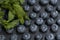 Symmetrical rows of blueberries on a black stone board with green mint petals. Stylish berry background. Summer berry
