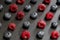 Symmetrical rows of blueberries and raspberries on a black stone board with green mint petals. Stylish berry background. Yummy