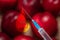 Syringe with chemical injection close-up. Blurred peaches in the background. The concept of GMO foods, vegetables and fruits