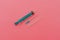 Syringe with green piston on a pink background. The concept of health.