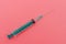 Syringe with green piston on a pink background. The concept of health.