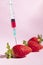 Syringe injecting artificial coloring into a fresh strawberry.