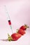 Syringe injecting artificial coloring into a fresh strawberry.