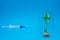 The syringe with the solution is directed at a green sprout in a glass flask on a blue background