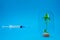 The syringe with the solution is directed at a green sprout in a glass flask on a blue background.