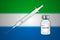 Syringe and vaccine vial on blur background with Sierra Leone fl