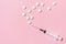 Syringe with white tablets as a injection and vaccination metaphor on pink background, flat lay, copy space