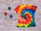 T-shirt painted in the style of tie dye with colors on a tinted wooden background. Flat lay