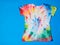 T-shirt painted in tie dye style on a blue background. Flat lay. The view from the top.