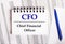 On the table are charts and reports, on which lie a blue pen and a notebook with the word CFO Chief Financial Officer