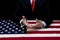 At a table covered with an American flag, a male businessman and politician holds out his hands for dialogue and suggestions