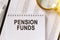 On the table are financial reports, a pen, a magnifying glass and a notebook with the inscription - PENSION FUNDS