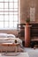 Table in front of a bed, stand with a plant and iron radiator in an industrial bedroom interior