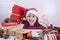 Table with gifts and a girl in a Christmas hat holding a gift wrapped in red paper