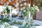 Table for guests, covered with a tablecloth, decorated with candles, transparent glass vases, fresh flowers and served with cutler