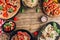 Table of italian meals on plates Pizza, pasta, ravioli, carpaccio. caprese salad and tomato bruschetta on rustic wooden background