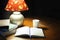 A table lamp, a white cup, an open book, some books, on a brown table