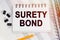 On the table is a pen and a notebook with inscriptions - SURETY BOND