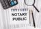 On the table are reports, a magnifying glass, a calculator, a pen, and a white notebook with the text NOTARY PUBLIC. Business