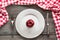 Table set with red apple on white plate with knife and fork with red checkered napkin.