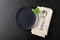 Table setting. Black plate, cutlery, napkin and basil leaves.