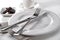 Table setting knife and fork on porcelain plate, linen cloth, bowl of chocolate pieces and cup with saucer on white background