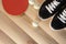 Table tennis racket, balls and black sneakers with white laces on a wooden background