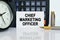 On the table there is a clock, a pen, a calculator and a business card on which the text is written - CHIEF MARKETING OFFICER