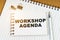 On the table there is a pen, clamps and a notebook with the inscription - WORKSHOP AGENDA