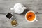 Table top view - brass tea caddy, white porcelain teapot and ceramic cup with silver spoon and hot amber drink, on gray wood desk.