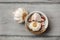 Table top view on garlic bulbs and peeled cloves in small ceramic bowl placed on gray wood desk.