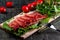 On the table is a wooden cutting board with sliced jamon, tomatoes and herbs