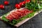 On the table is a wooden cutting board with sliced jamon, tomatoes and herbs