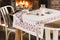 Tablecloth with Red Floral Design on Table near Blazing Fireplace