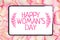 A tablet on a background of petals of pink roses with an abstract inscription - Happy Women`s Day with branches on the sides