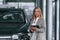 With tablet in hands. Woman in formal clothes is in the car dealership