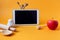 A tablet with kitchen equipment and a red apple on a yellow background  side view-the concept of conducting online cooking courses