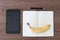 Tablet, notebook, pen and a banana on a wooden table. Image concept for journalism, liar and fake news, problems of hoaxes and tr