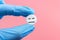 Tablet with a sleeping smiley in a hand in a medical glove on a pink background. Sleeping pills for insomnia