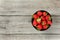 Tabletop view, small black ceramic bowl with strawberries, gray wood desk under. Space for text on left side