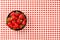 Tabletop view, small black ceramic bowl of strawberries on red chequered gingham tablecloth