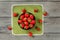 Tabletop view, small black ceramic bowl, with strawberries, some of them spilled on green tablecloth under