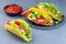 Taco shells with lettuce, ground beef meat,  mashed avocado, tomato, red onion and jalapeno pepper, on stone plate, horizontal,