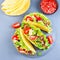 Taco shells with lettuce, ground beef meat,  mashed avocado, tomato, red onion and jalapeno pepper, on stone plate, square format