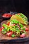 Taco shells with lettuce, ground beef meat,  mashed avocado, tomato, red onion and jalapeno pepper, on wooden board, vertical,