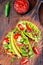 Taco shells with lettuce, ground beef meat,  mashed avocado, tomato, red onion and jalapeno pepper, on wooden board, vertical, top