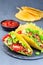Taco shells on stone plate, with lettuce, ground beef meat,  mashed avocado, tomato, red onion and jalapeno pepper, vertical,